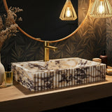 A fluted Calacatta Amber Viola marble vessel sink sits atop a wooden vanity with golden faucet details.