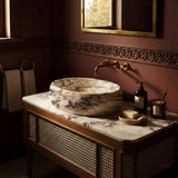 This luxurious bathroom sink features a Calacatta Amber Viola marble vessel set on a rattan-fronted wooden console.