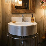A fluted Carrara marble sink with a chrome base enhances the warm, elegant ambiance of a luxury powder room.