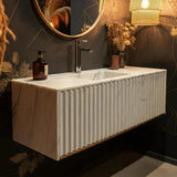 This fluted Carrara marble vanity sink floats elegantly on a dark feature wall, blending modern luxury with artisanal detail.