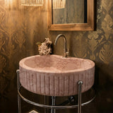 The image features a fluted pink marble oval sink elegantly styled with chrome legs in a luxurious, vintage-inspired powder room.
