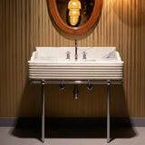 This white Carrara marble sink features fluted edges and a bold veining pattern, set atop a sleek chrome frame.